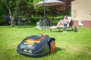 Black and orange robotic lawn mower in residential homeowners lawn cutting grass and being controlled digitally in Springfield, IL.