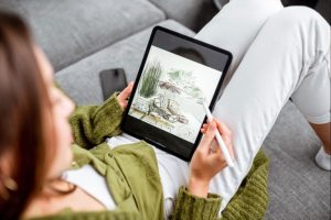 Woman in a green sweater and white pants holding an iPad device and drawing a digital landscape design on a landscaping software in Springfield, IL.
