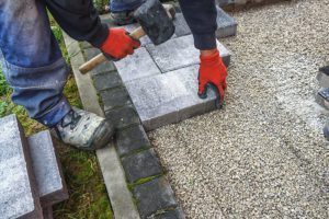Contractor in a blue work uniform and red gloved using a hammer to install concrete paving stones onto a patio in Springfield, IL.